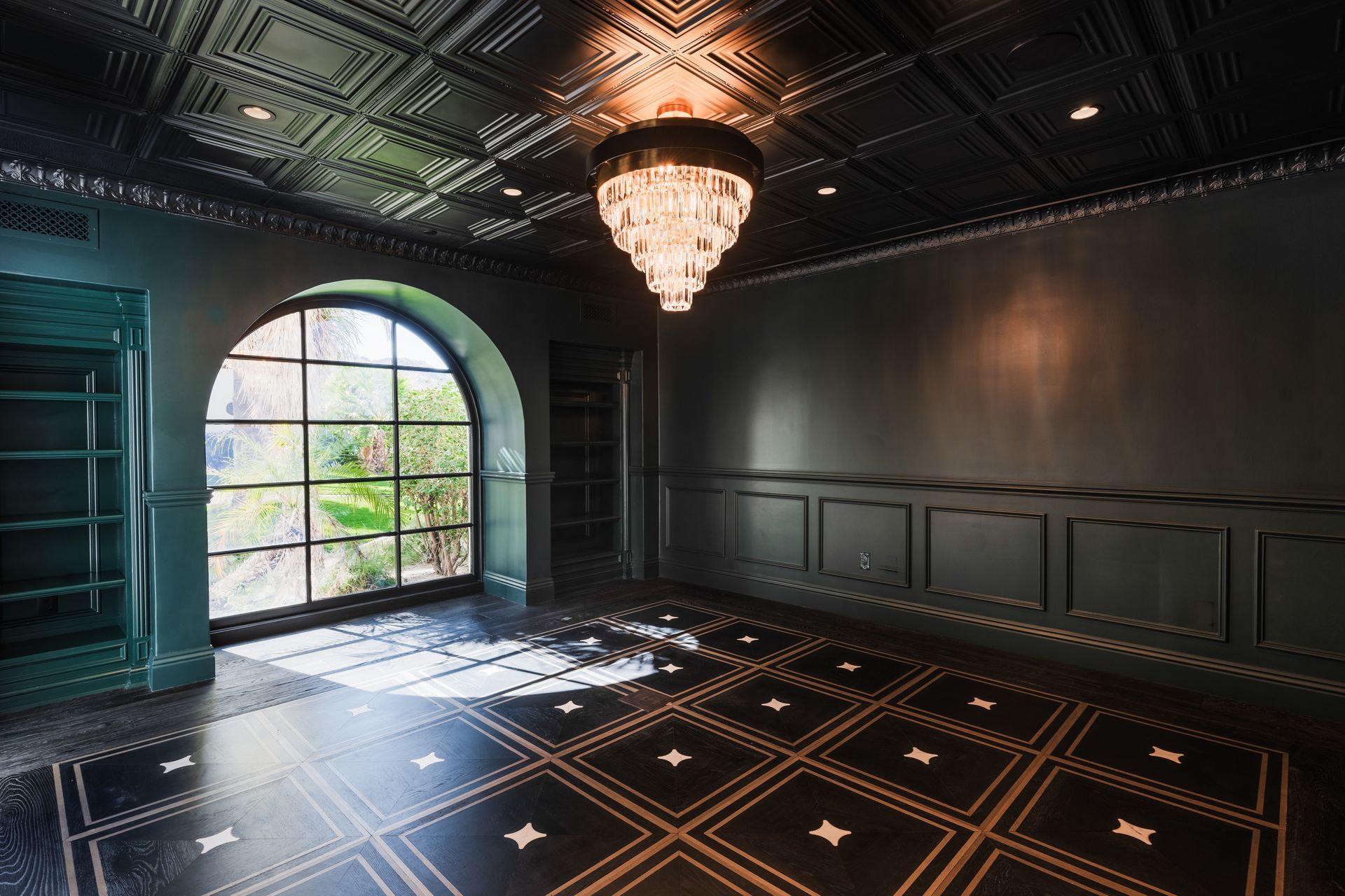 Luxurious room with dark walls, patterned floor, arched window, and crystal chandelier.