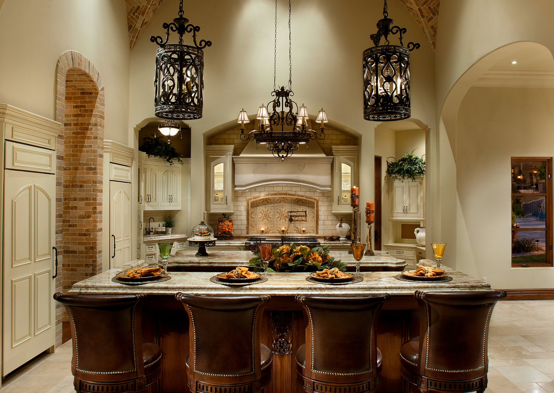 Ornate kitchen with large island, multiple chandeliers, and a brick archway.