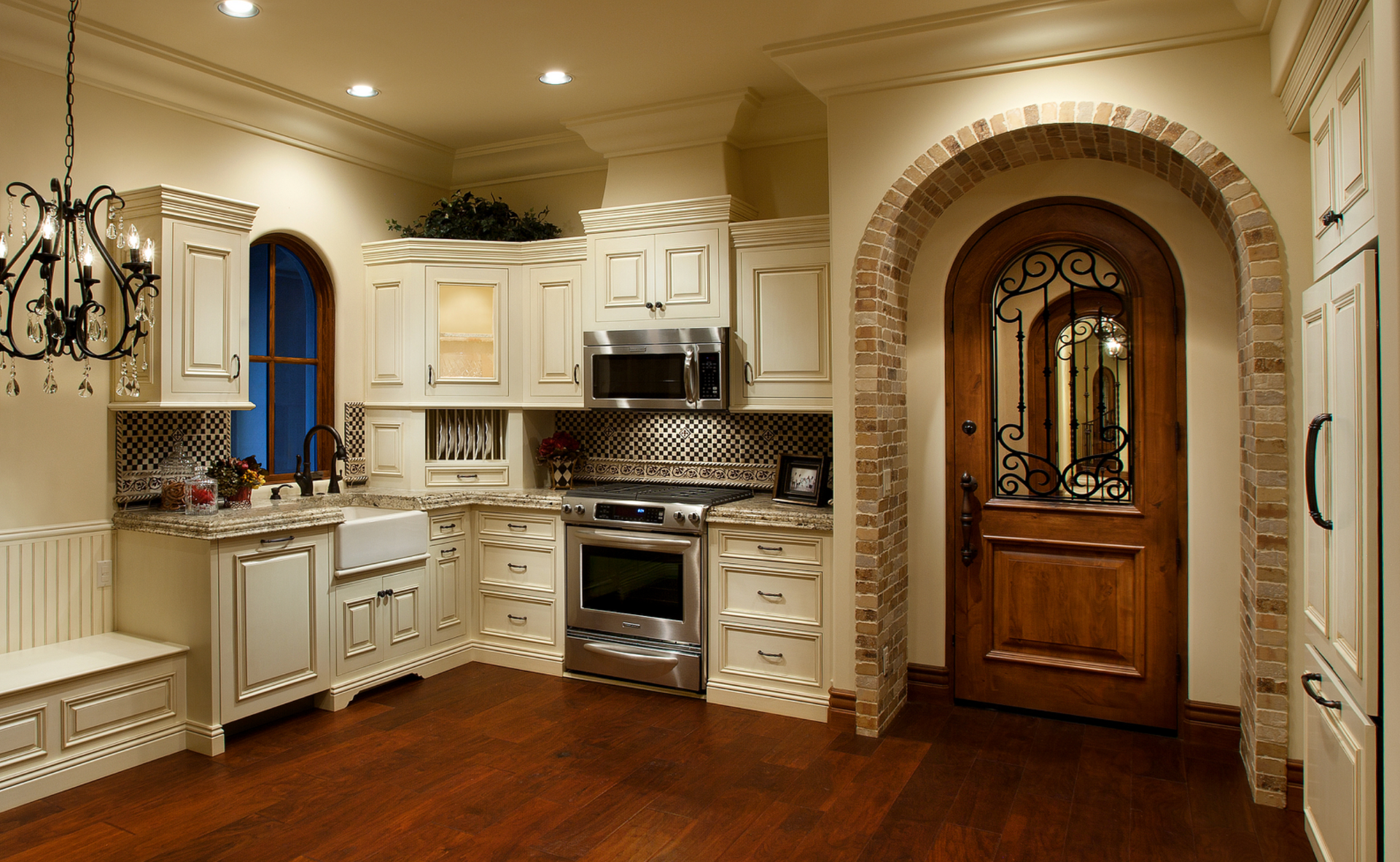 Luxurious kitchen with arched doorway, light-colored cabinetry, stainless steel appliances, and dark wooden floors.