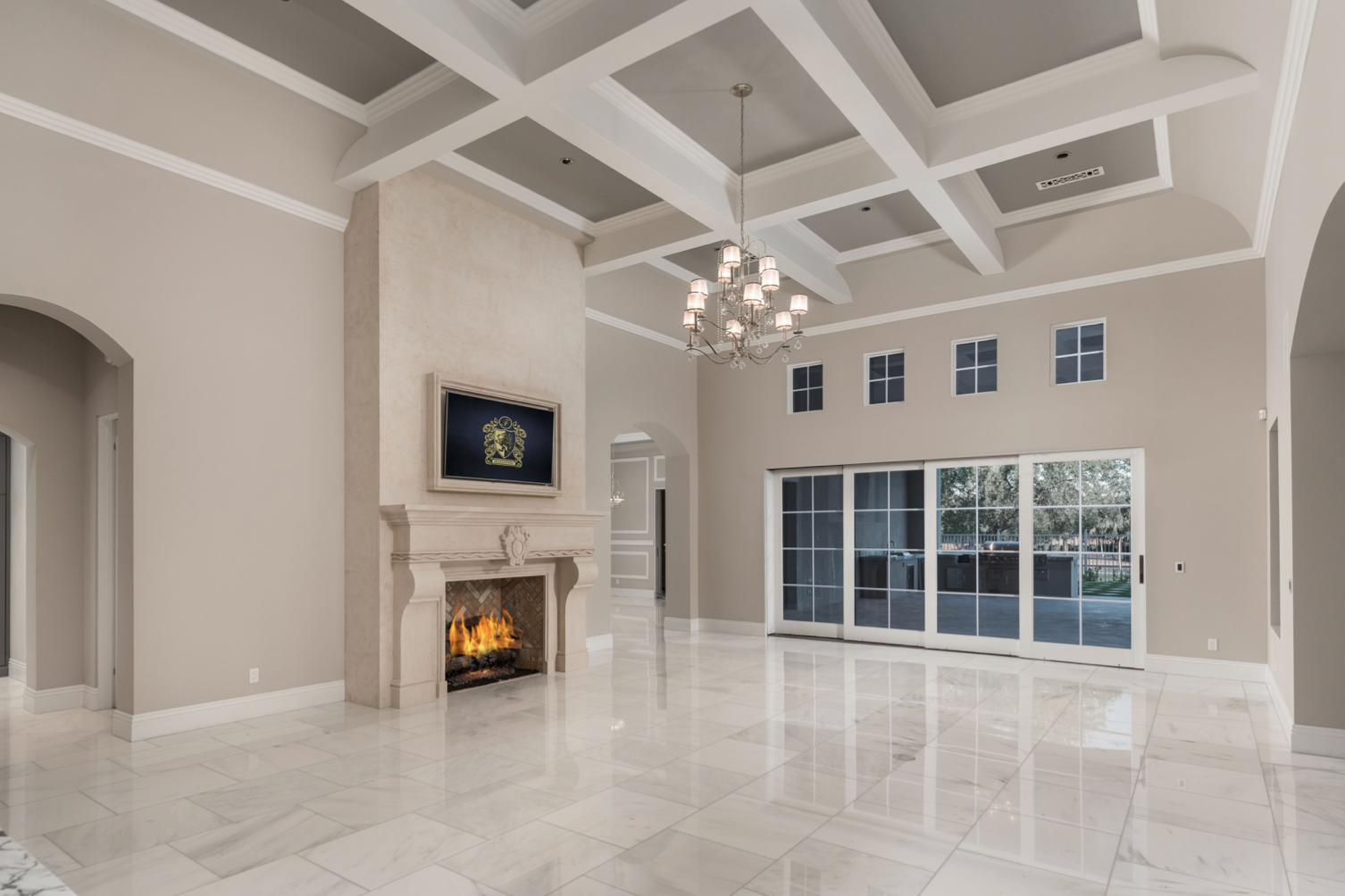 Spacious living room with fireplace, sliding glass doors, coffered ceiling, and marble flooring.