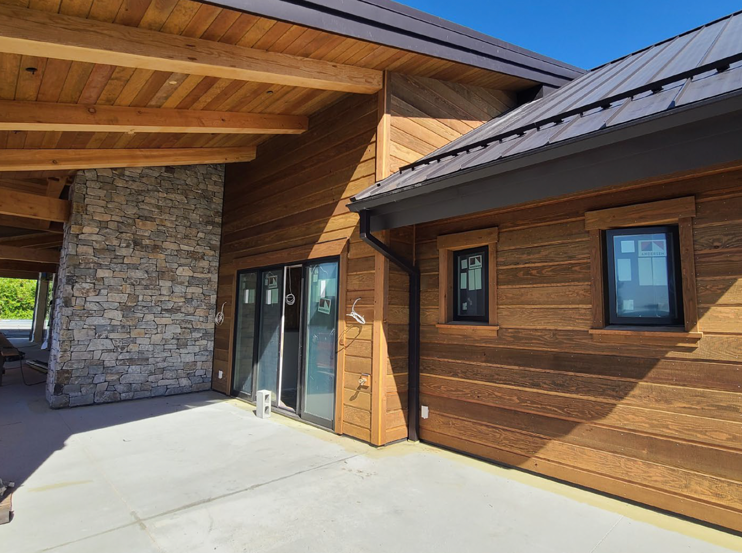 Exterior view of a modern house with wood siding, stone accents, and dark roof.