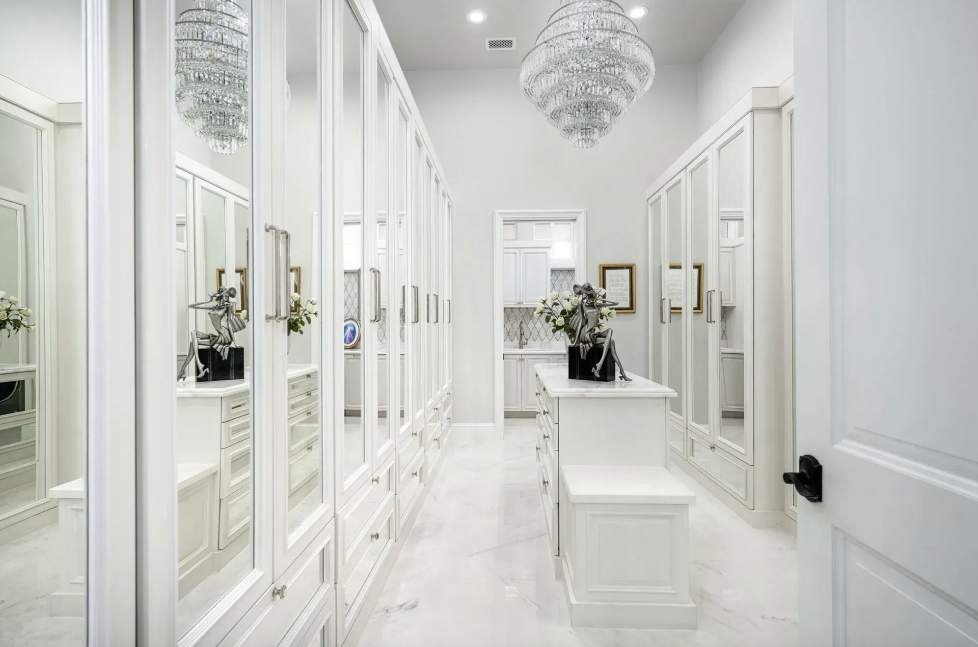 White walk-in closet with mirrored doors, a central island, and crystal chandeliers.