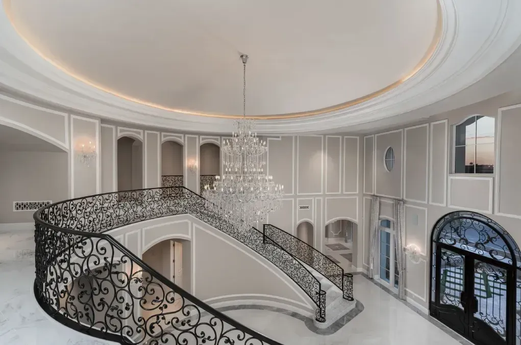 Luxury home interior featuring an elegant curved staircase, chandelier, and custom architectural details