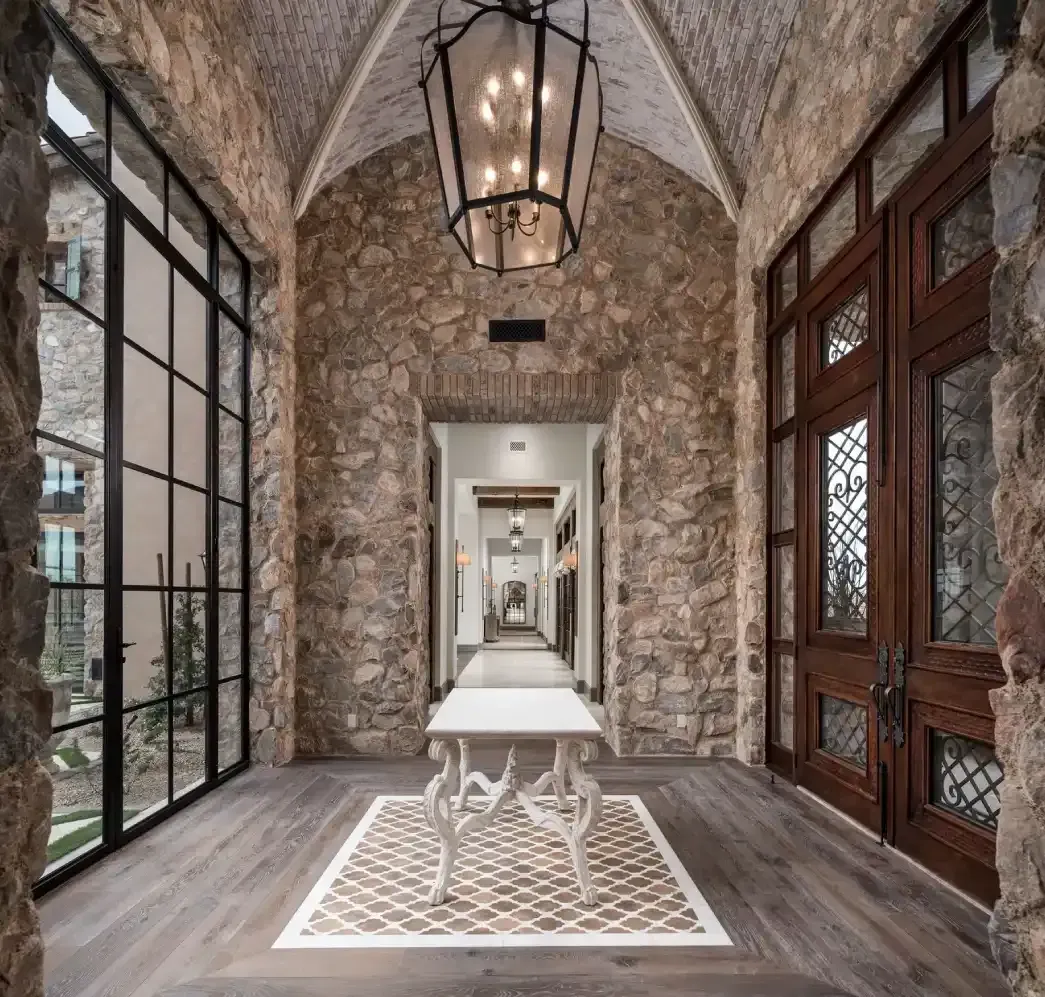 Luxury home entrance with stone walls, vaulted ceiling, and large windows