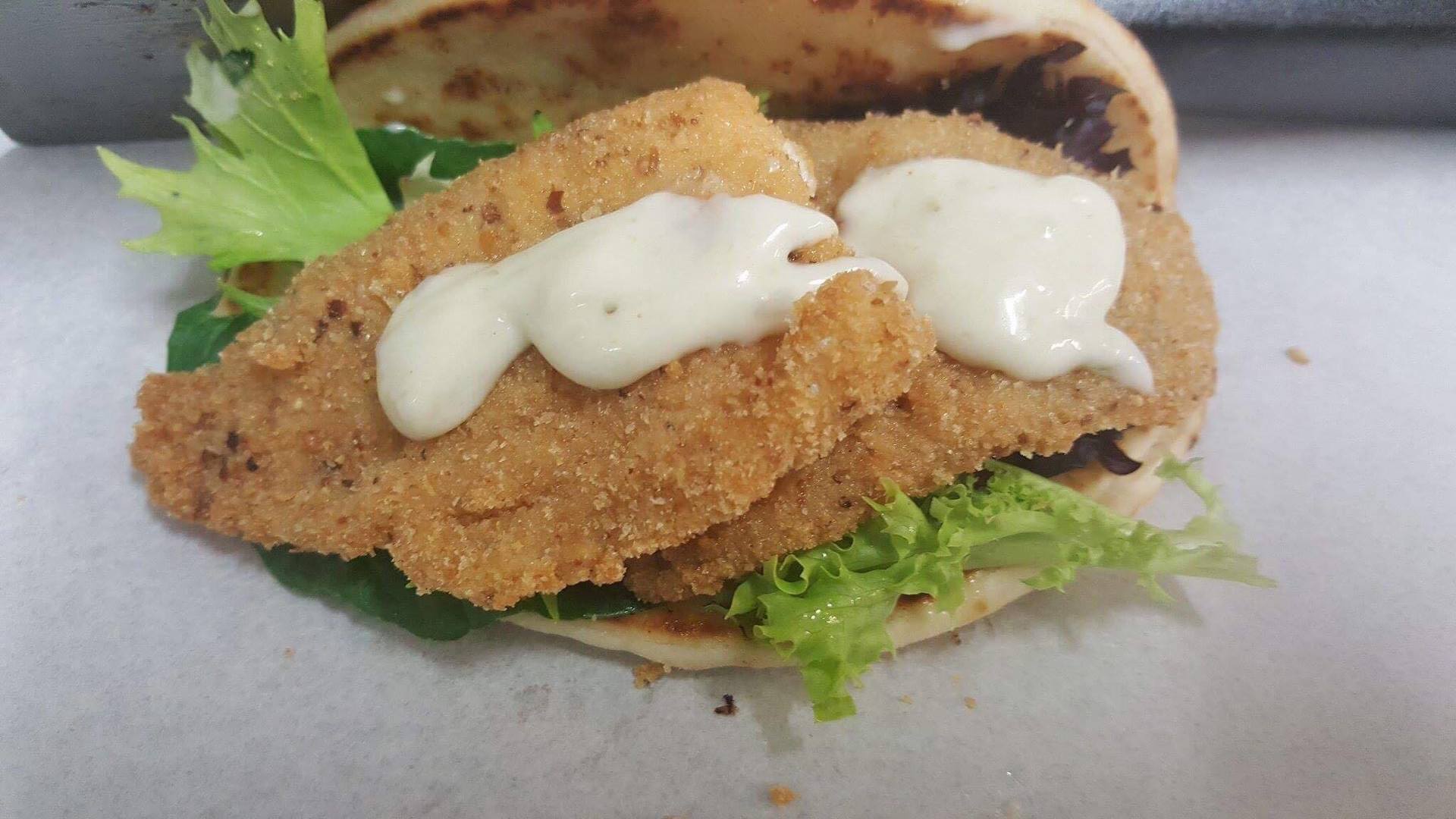 Breaded sandwich with lettuce and creamy sauce on a bun, close-up on a white plate