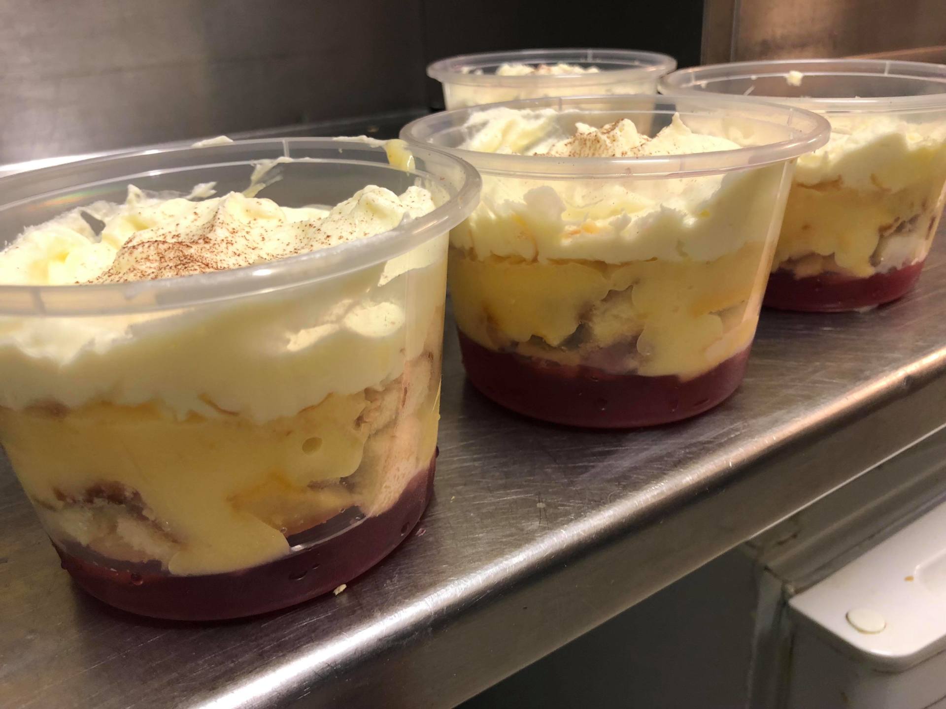 Three clear cups of layered dessert with whipped topping and red fruit sauce on a metal tray.