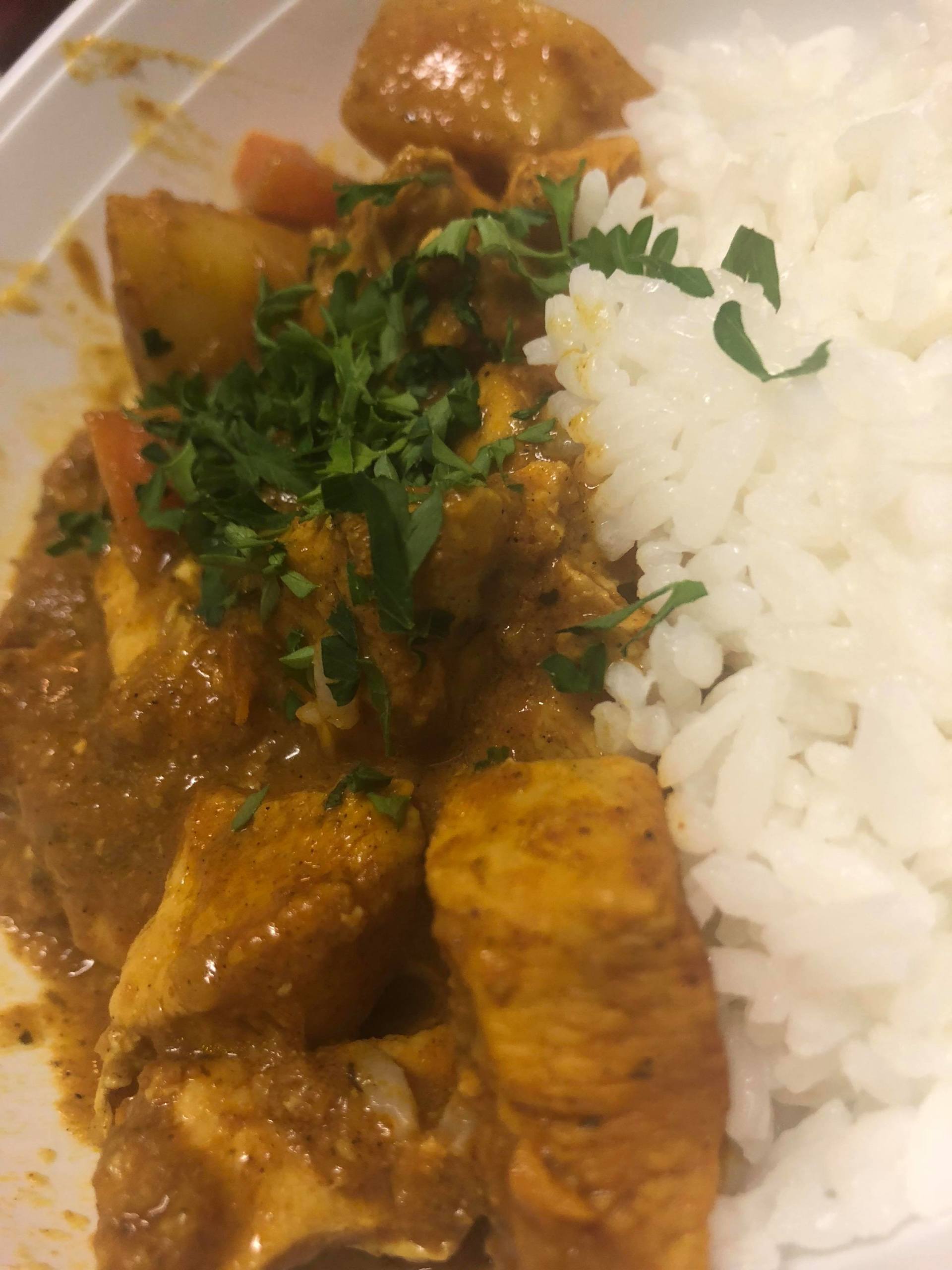 Plate of white rice with saucy chicken curry, garnished with chopped herbs.