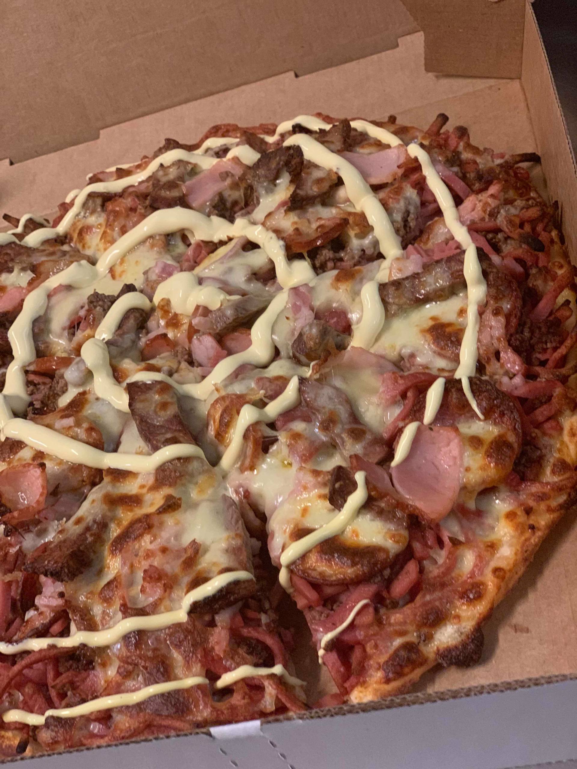 Pizza with sausage, bacon, and drizzled white sauce in a takeout box
