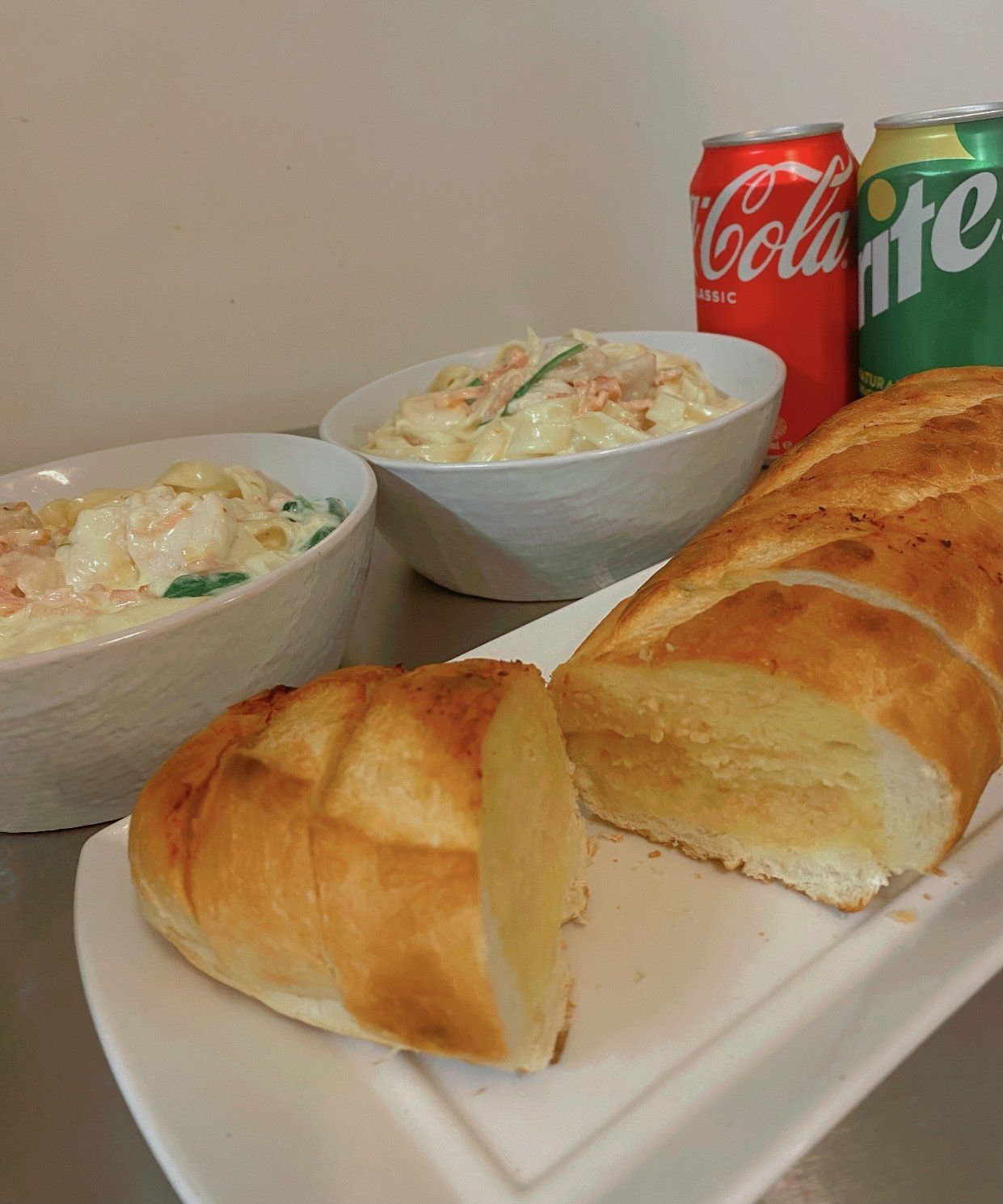 Breakfast spread with sliced bread, two bowls of creamy salad, and Coke and Sprite cans in the background