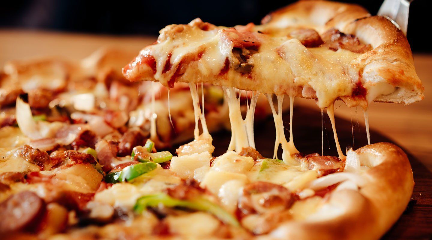 Slice of cheesy pizza being lifted, with melted cheese stretching from the pie.