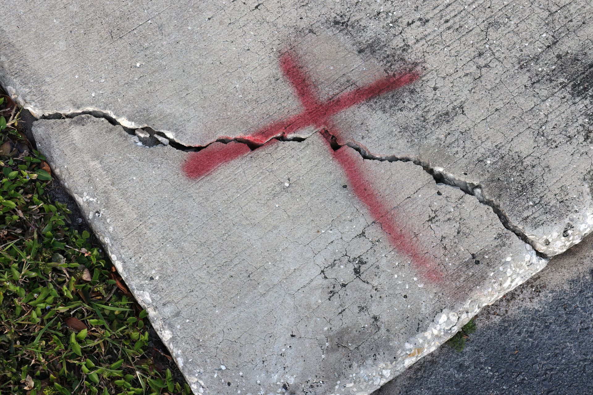 A cracked sidewalk with a red cross painted on it.