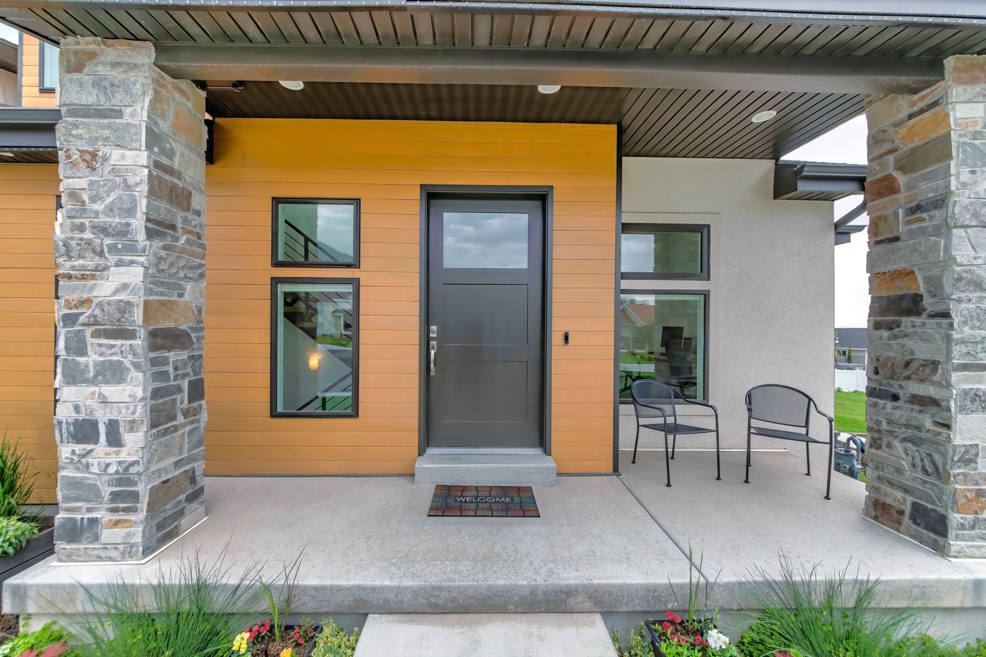 The front door of a house with a porch and chairs.