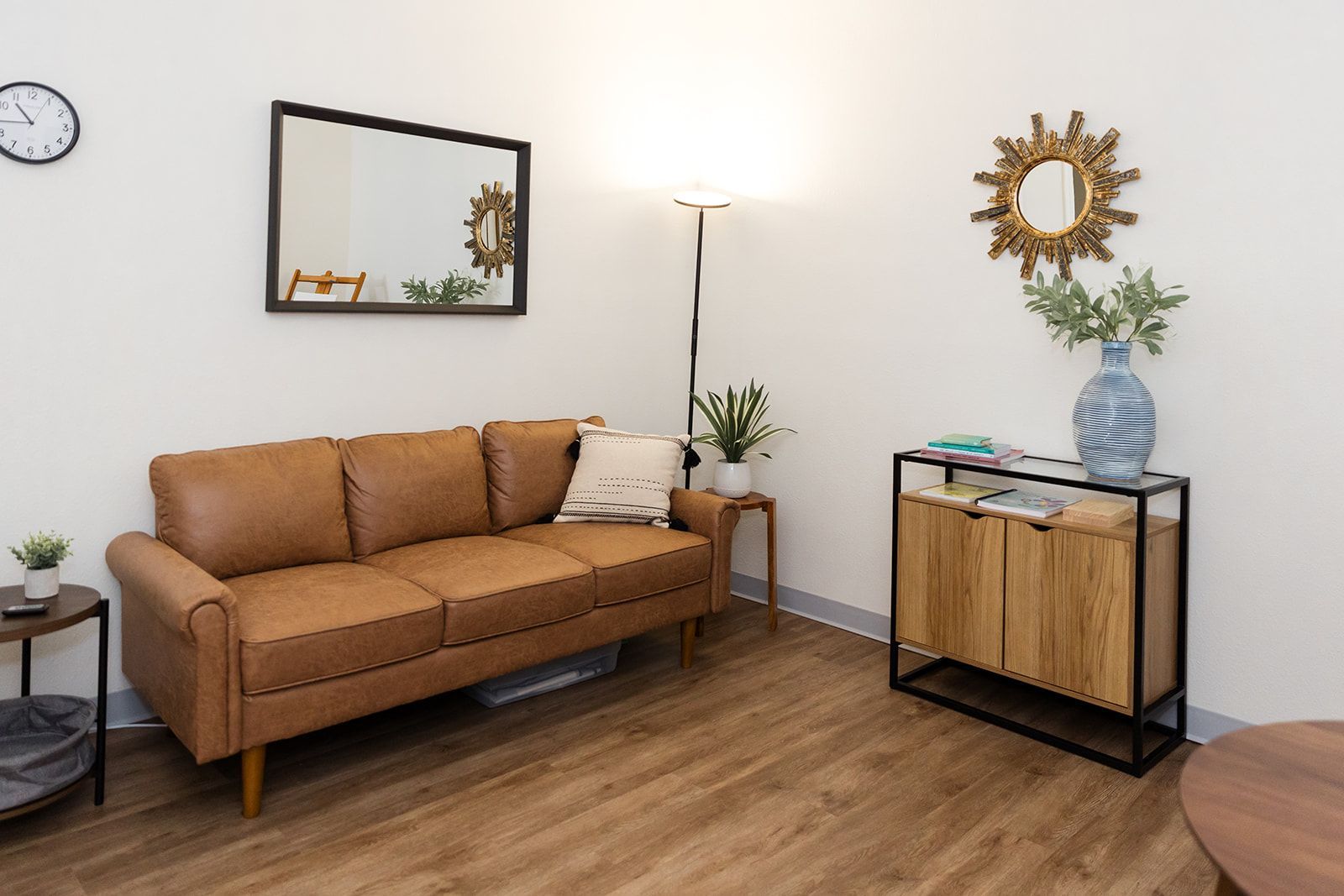 Cozy living room with tan sofa, floor lamp, mirror, side table, and wood console on hardwood floors