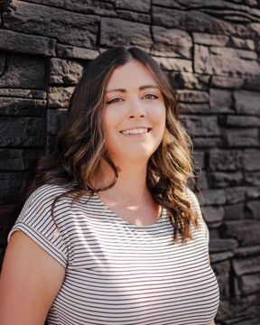 Smiling woman in striped shirt standing before a dark stone wall