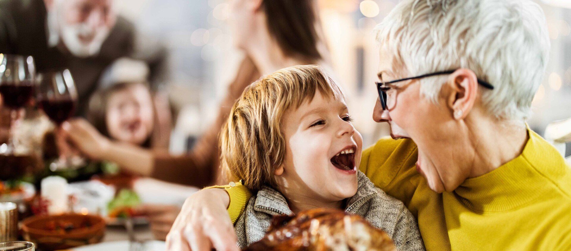 Older adult smiling at a laughing child during a family meal