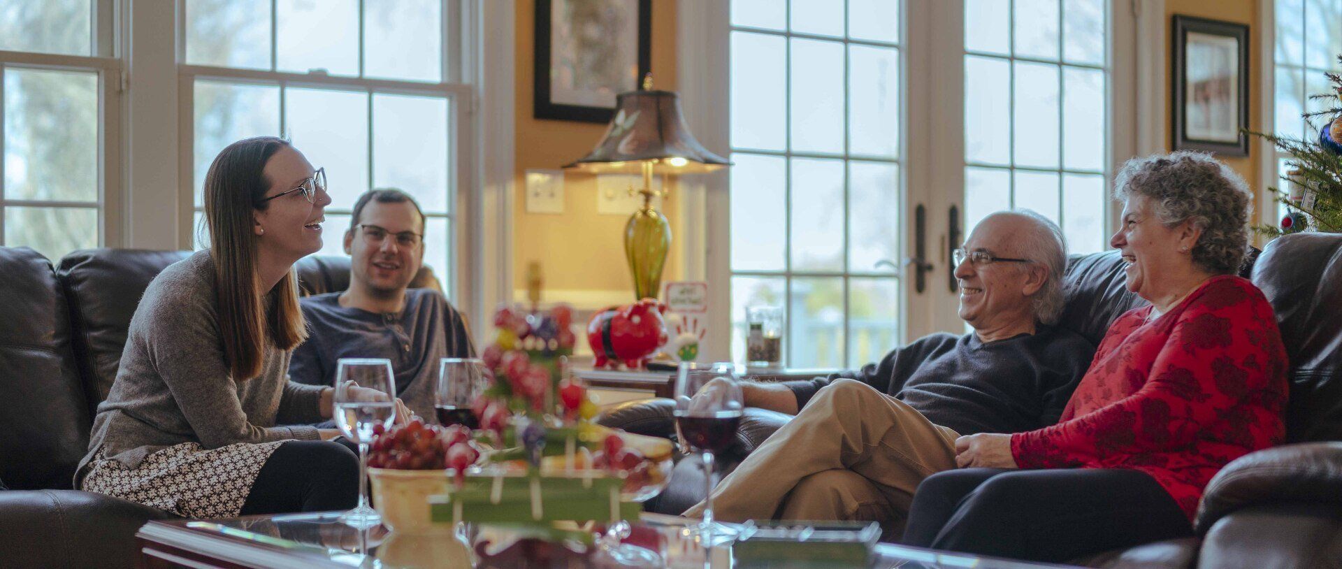 Four people chatting on sofas in a sunlit living room with wine glasses and a coffee table