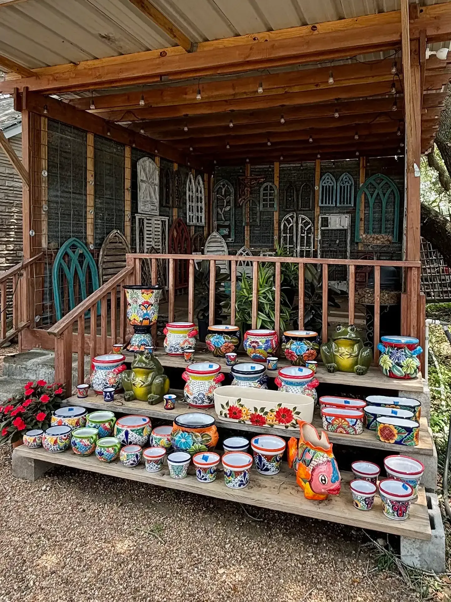 Colorful painted pots and decorative bowls displayed on steps outside a wooden porch and fence
