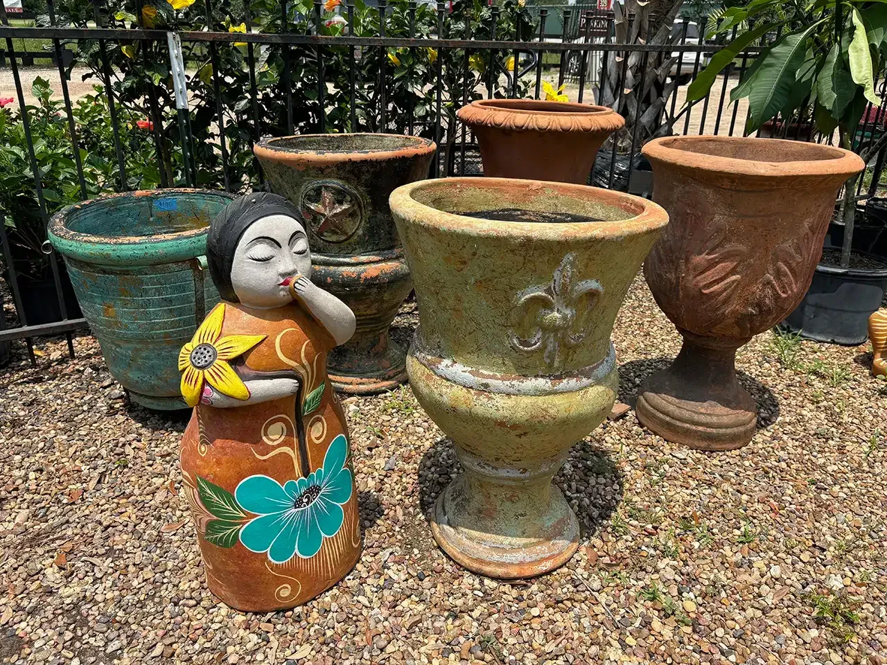 Outdoor display of colorful ceramic planters and a decorative figurine in a gravel garden area