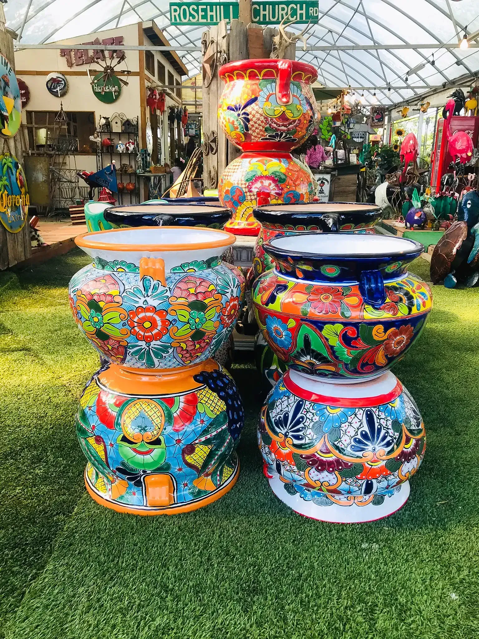 Colorful painted ceramic pots are displayed outdoors on artificial grass in a garden market.