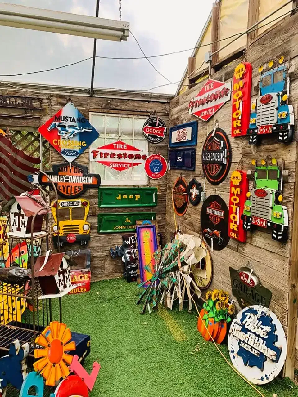 Colorful wall of assorted signs and decor in a narrow outdoor market alley with artificial grass floor