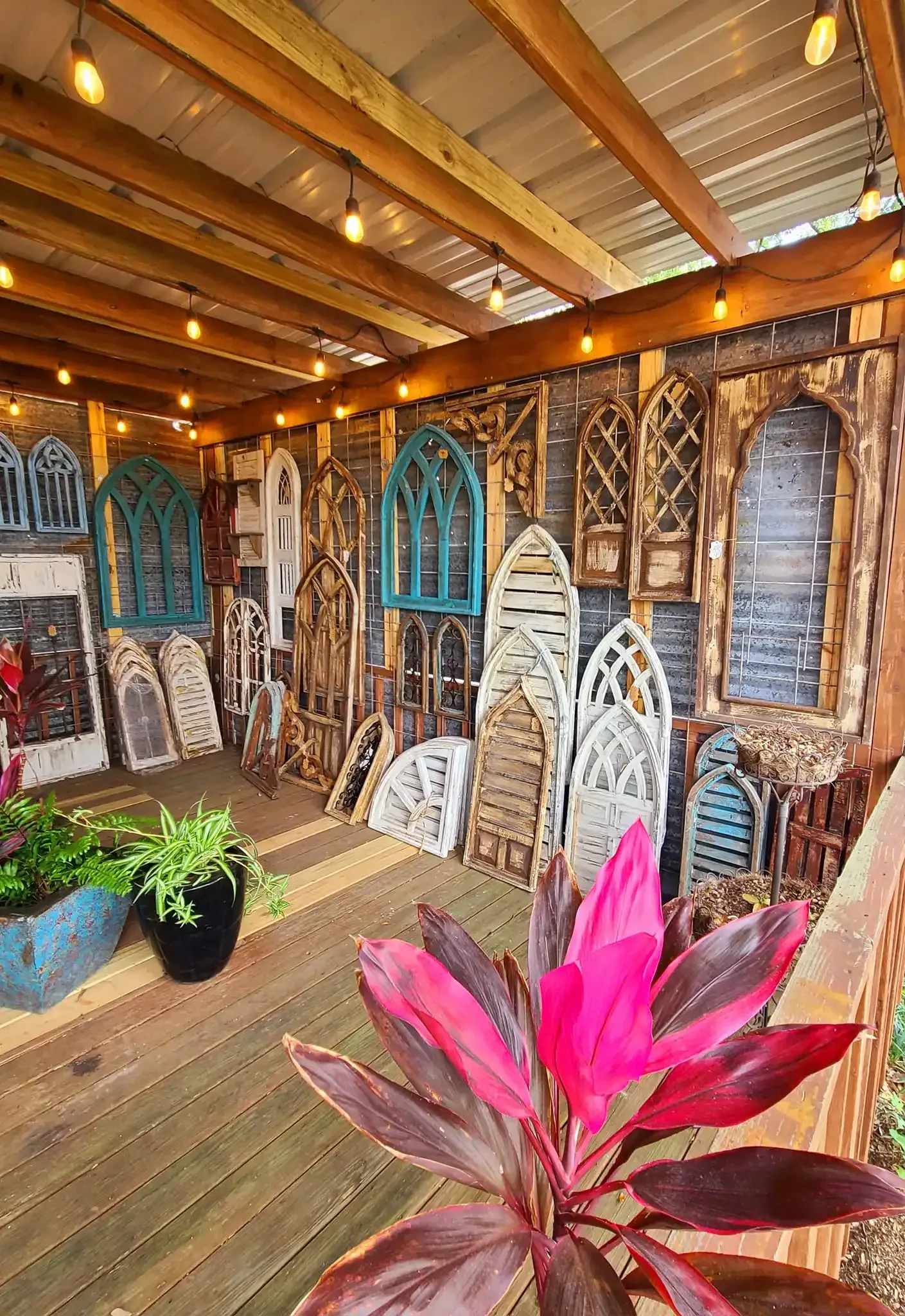 Colorful rustic patio with carved wall decor, hanging lights, and pink tropical plants