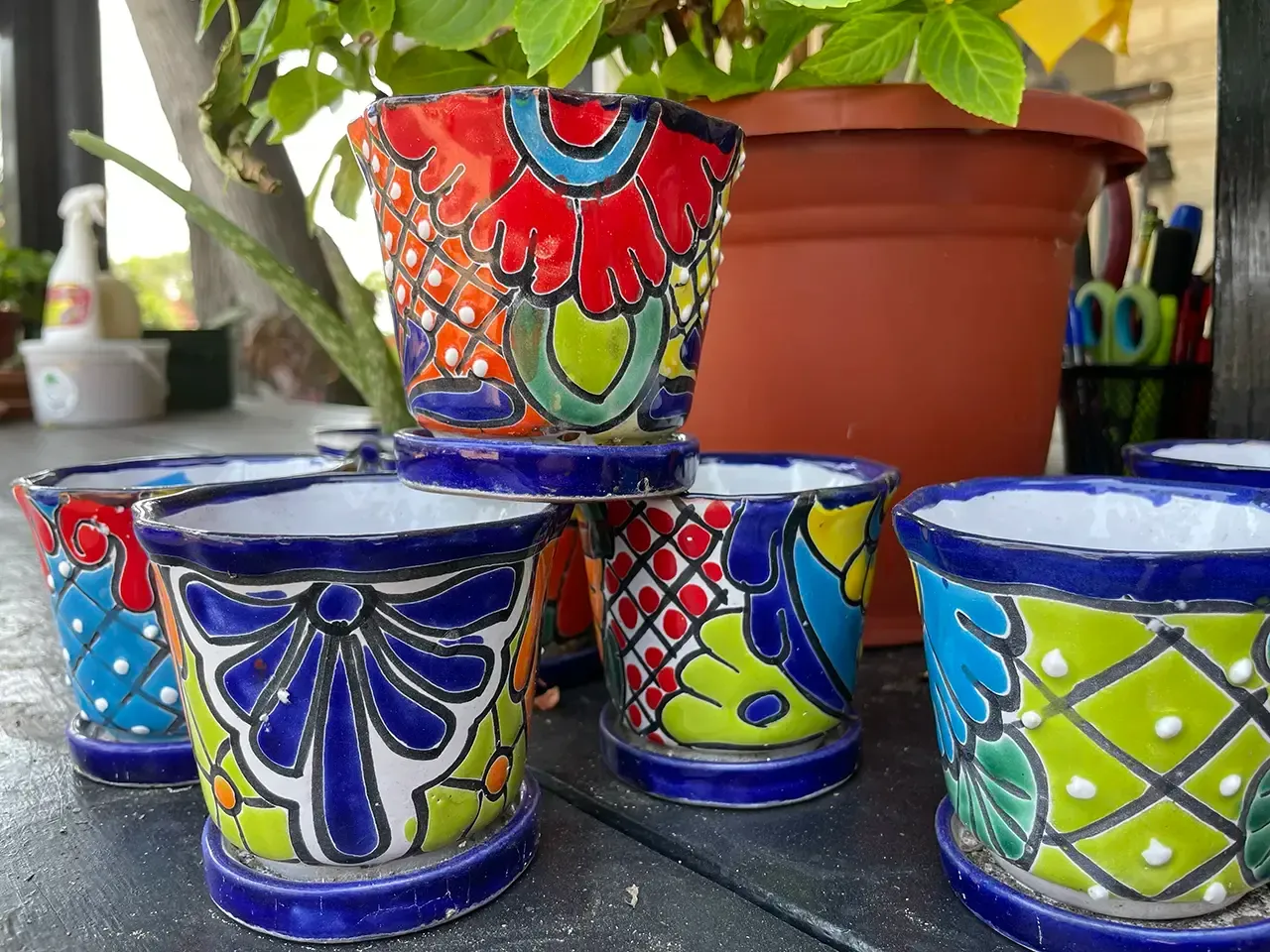 Colorful hand-painted ceramic pots with blue, red, and green patterns on a table with plants
