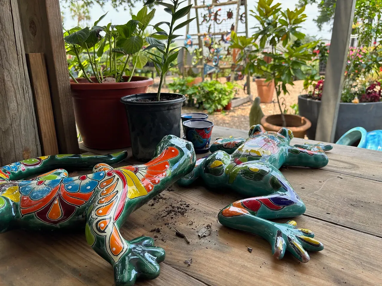 Colorful beaded lizard sculpture on a wooden table, with potted plants in the background.