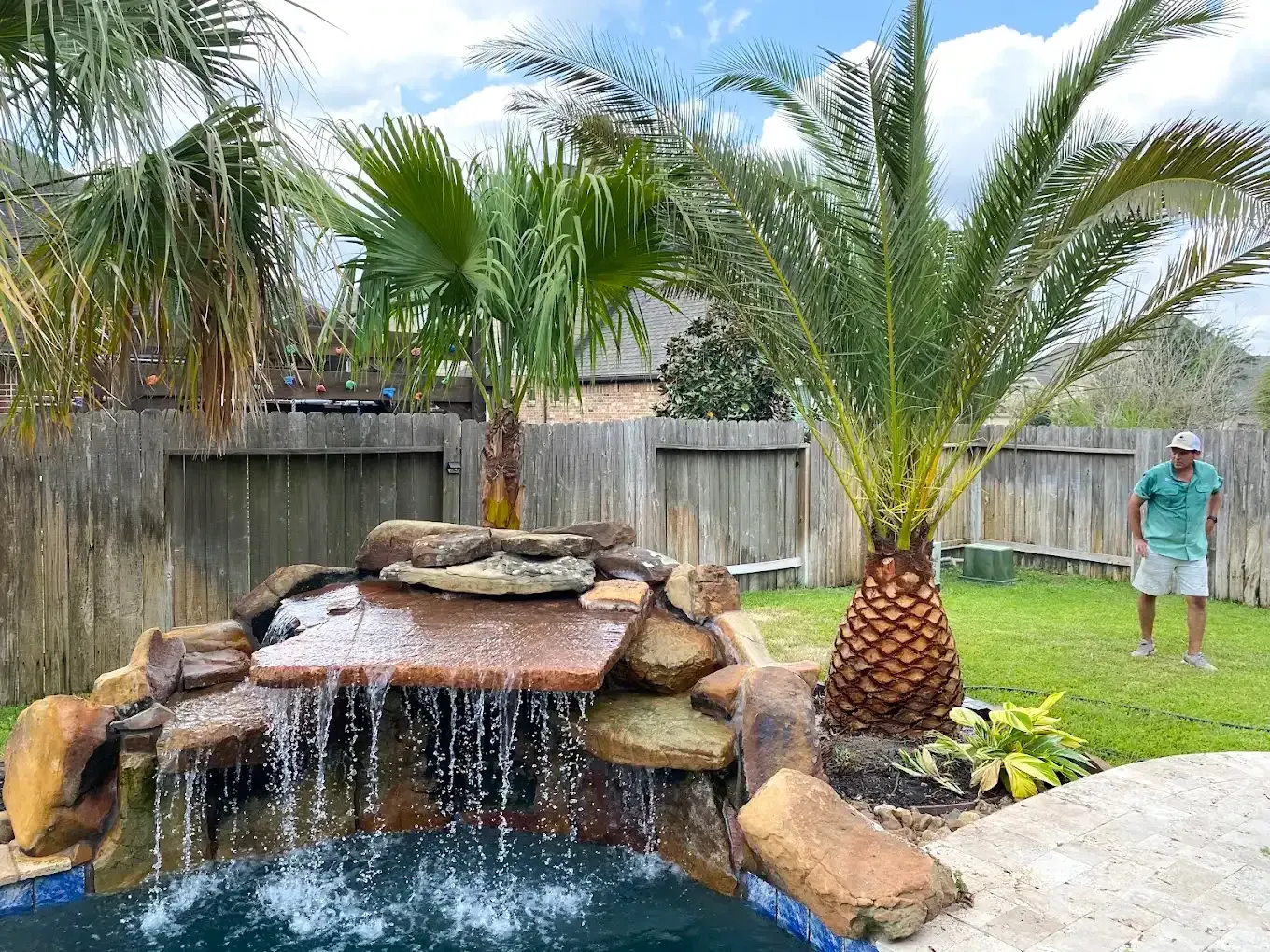Backyard waterfall pond with palm trees and a person standing near the lawn