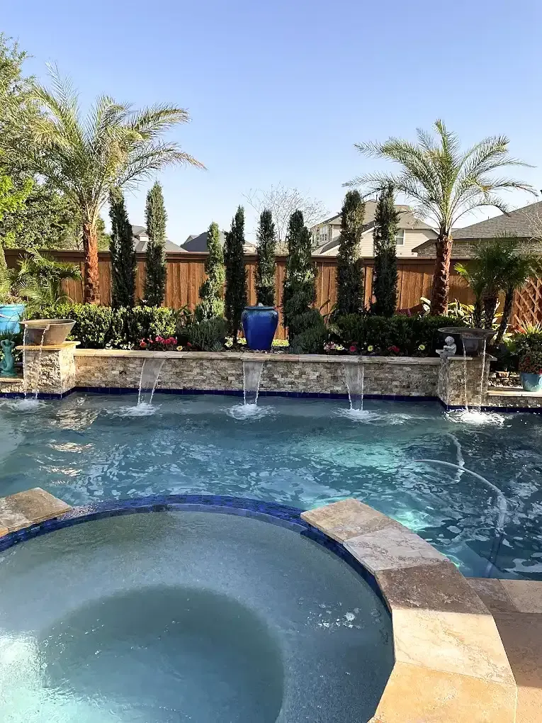 Backyard pool with fountain jets, spa, palm trees, and a tiled patio in bright sunlight