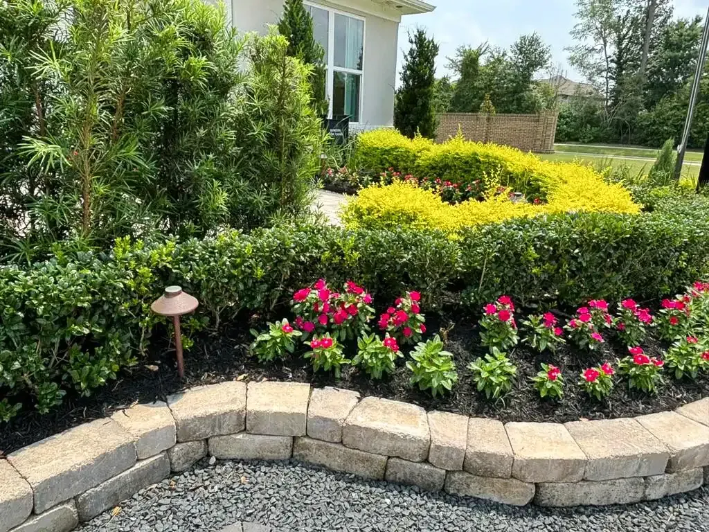 Landscaped garden with pink flowers, hedges, stone edging, and a house in the background