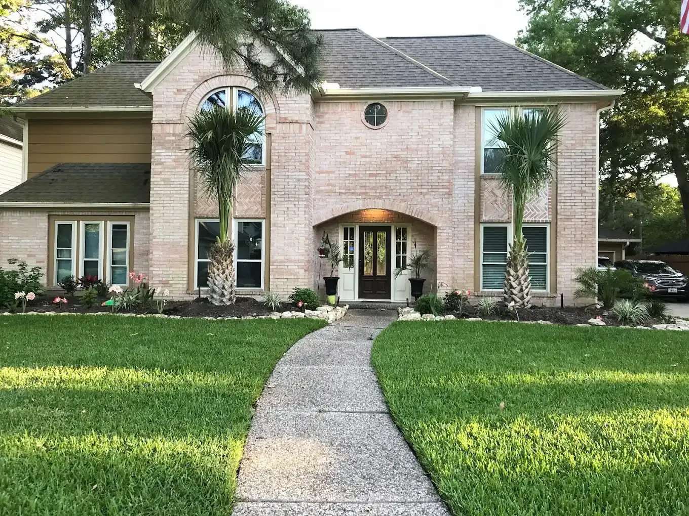 Two-story brick house with a curved walkway, green lawn, and trees in front