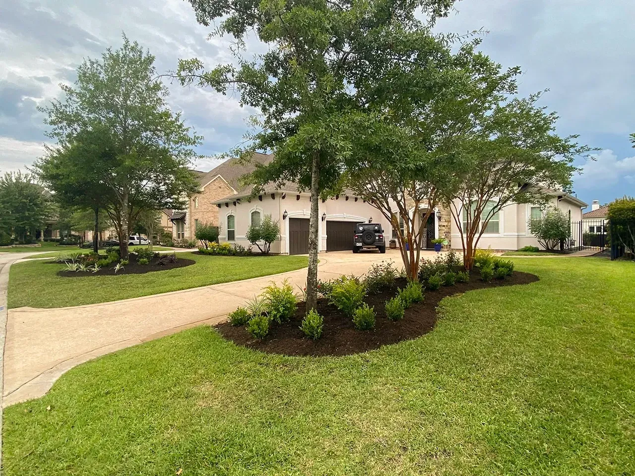 Suburban house with a curved driveway, manicured lawn, and trees under a cloudy sky