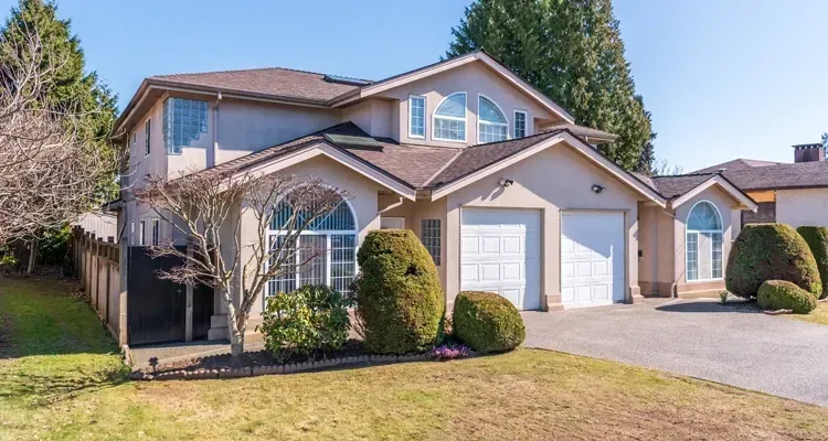 Two-story beige house with arched windows and a two-car garage, on a grassy lawn.