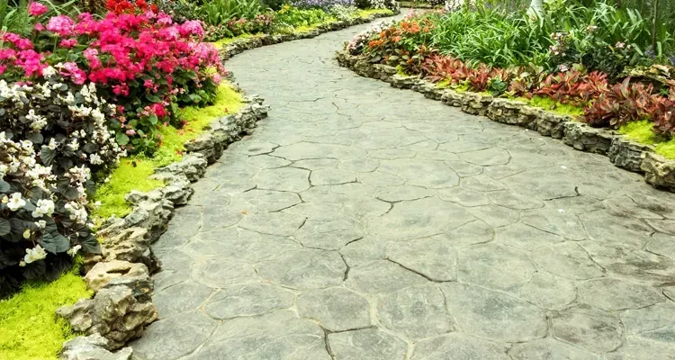 Stone pathway through a garden with pink and red flowers, and green plants.
