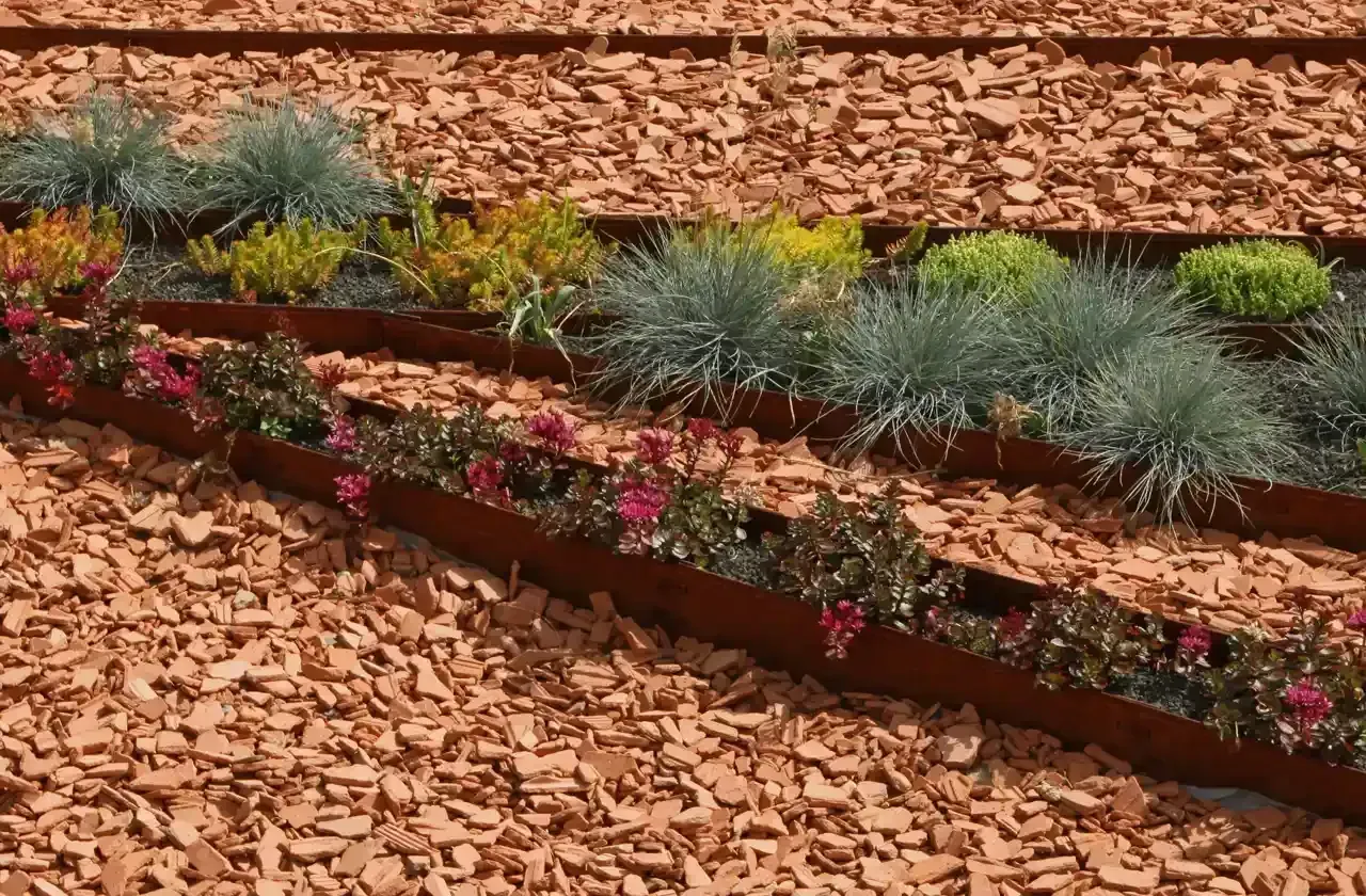 Landscape bed with tiered Corten steel planters, filled with colorful plants and wood chips.