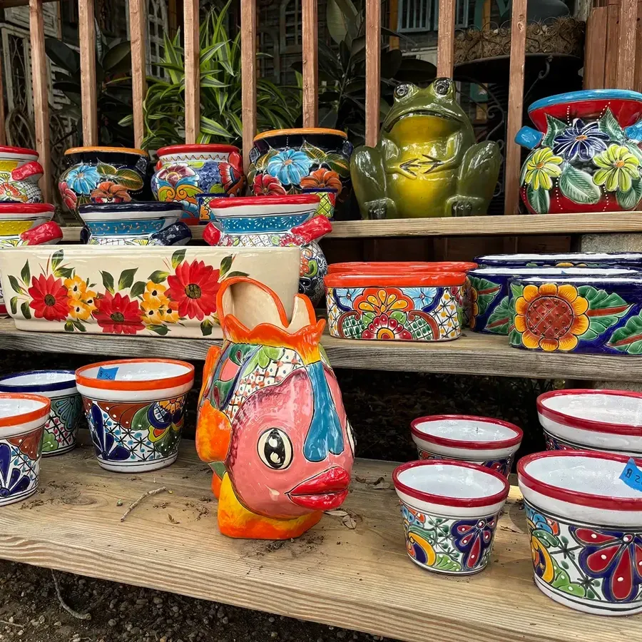 Colorful ceramic pots and a frog statue displayed on a wooden shelf outdoors.