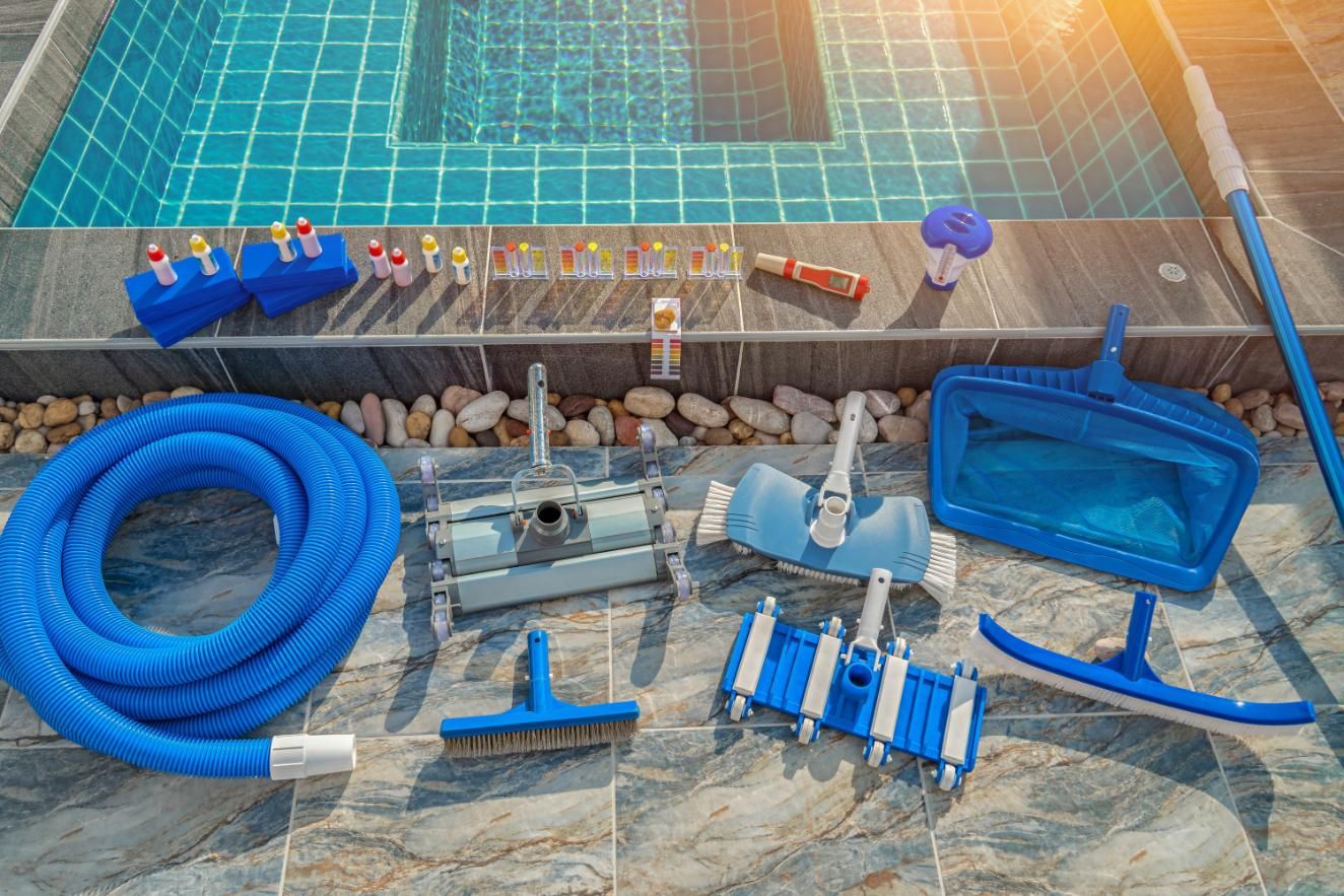 Pool cleaning supplies arranged on tile: blue hose, brushes, skimmers, test kit, and pool.