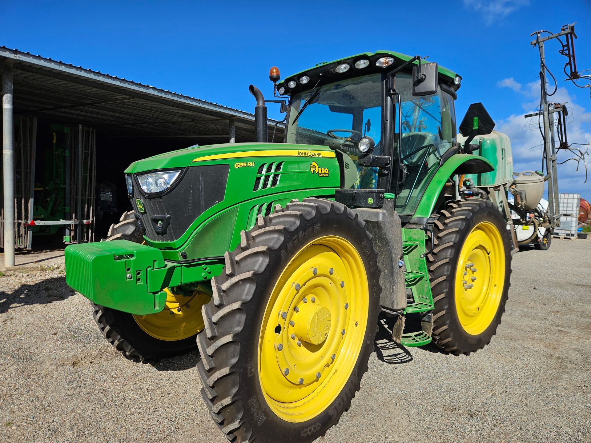 Green John Deere tractor with yellow wheels parked outside a farm building on a sunny day
