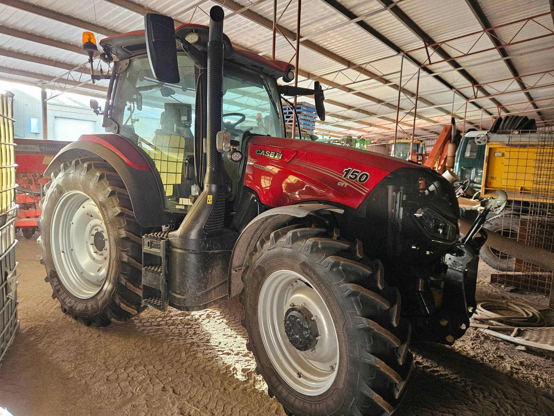 Red tractor parked inside a barn or equipment shed, with large tires and a front loader.