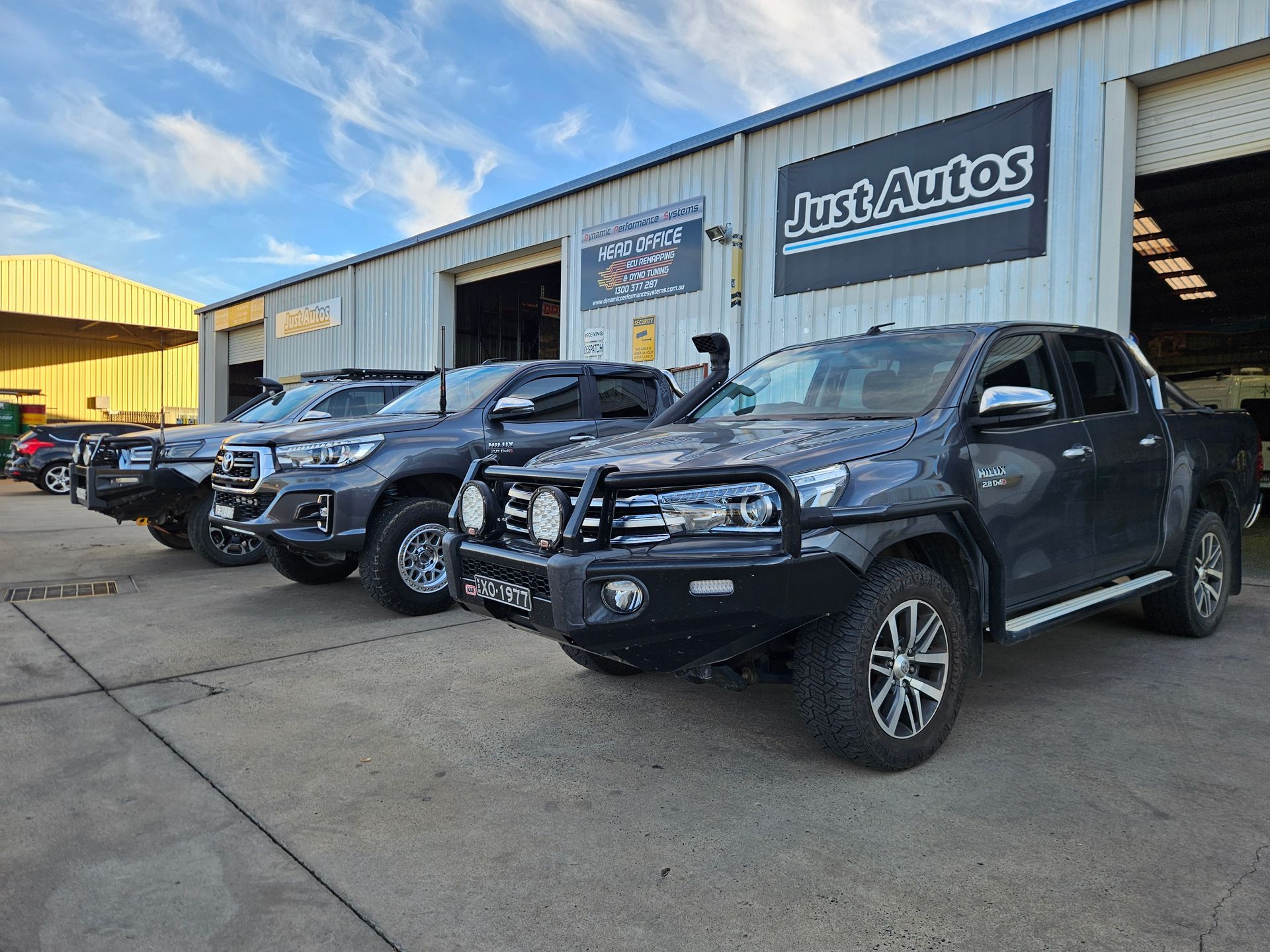 Black pickup trucks lined up outside a Just Autos dealership building.