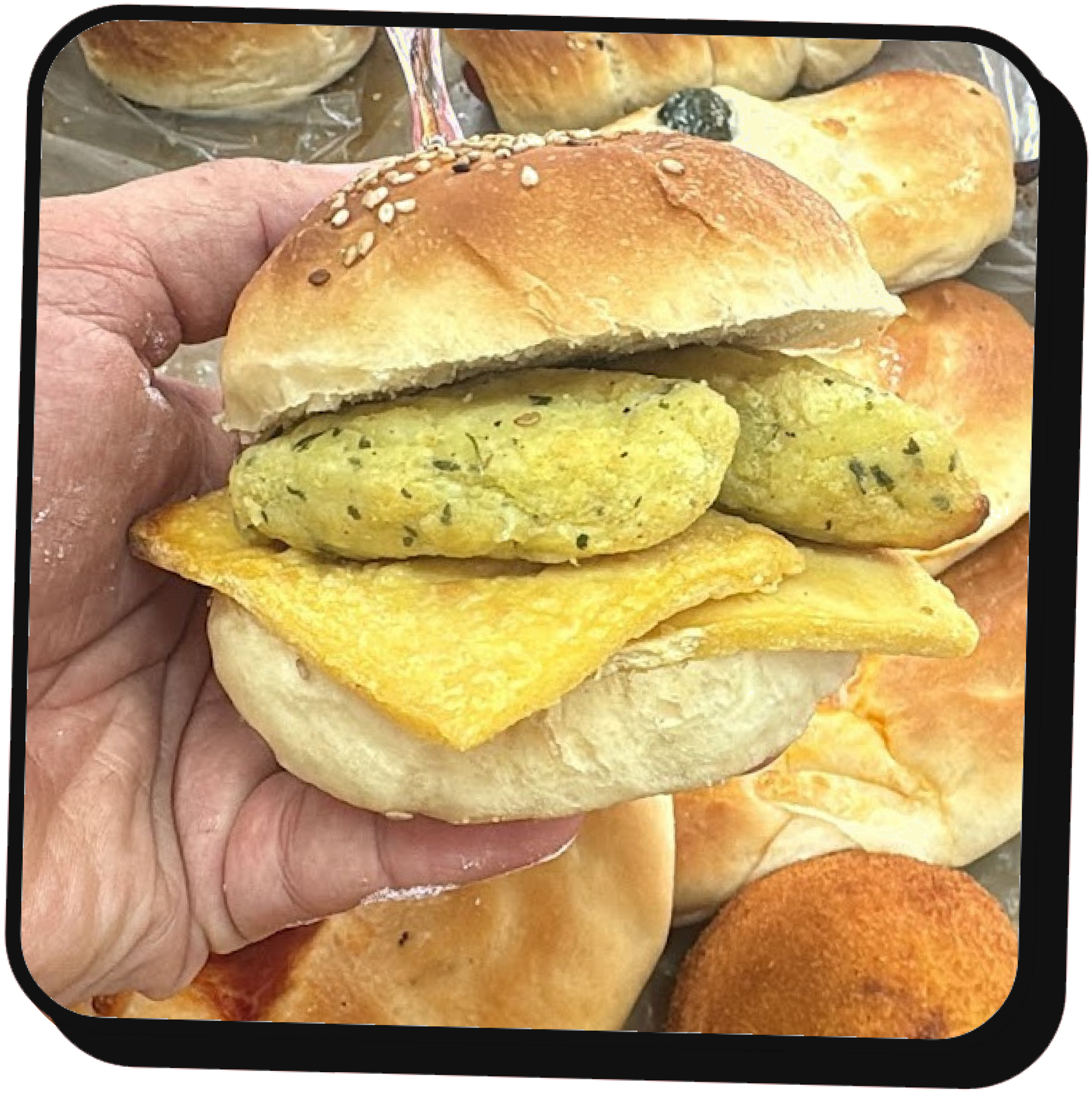 Mano che regge un panino farcito con ripieni saporiti e uno strato di formaggio giallo, con panini da forno sullo sfondo.