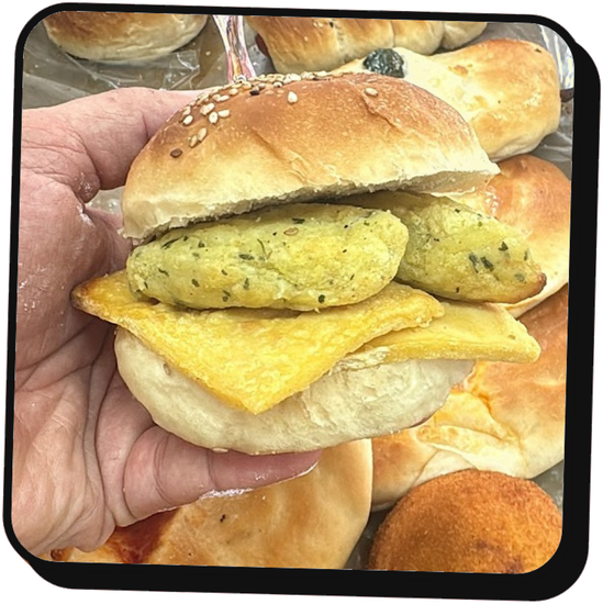 Una mano che regge un panino farcito con uova fritte e tortini alle erbe, con altri panini sullo sfondo.