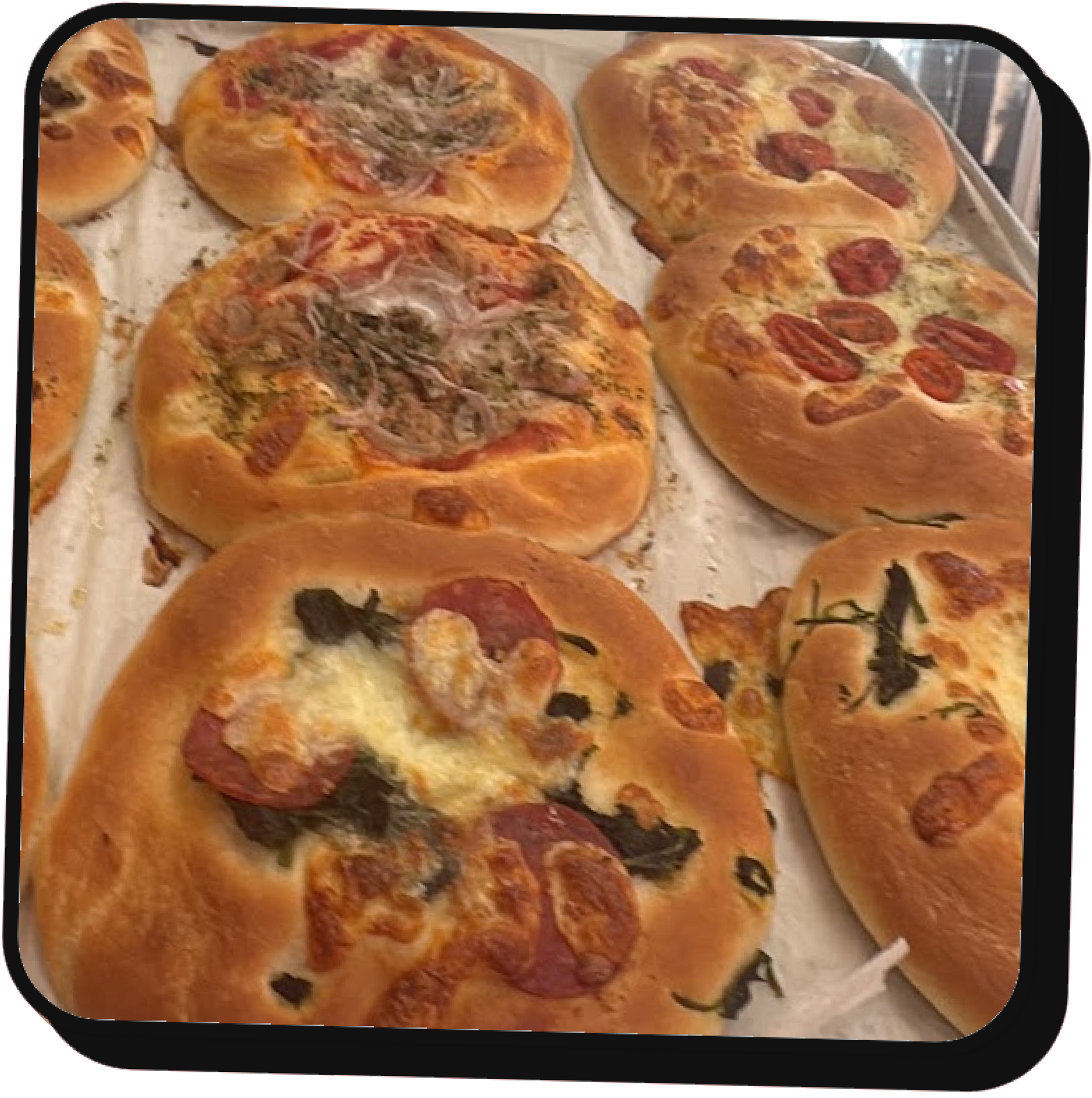 Vassoio di mini pizze assortite su carta da forno, con formaggio, salame piccante e funghi.