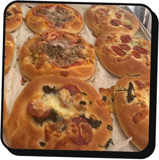 Vassoio di mini pizze assortite e panini salati su carta da forno, dorati e appena sfornati.