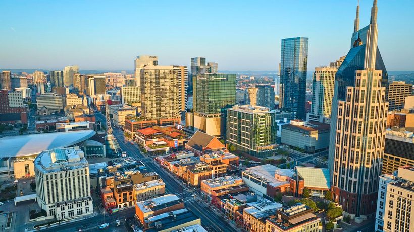 Downtown city skyline at sunset with modern buildings and a tall cathedral-like tower.