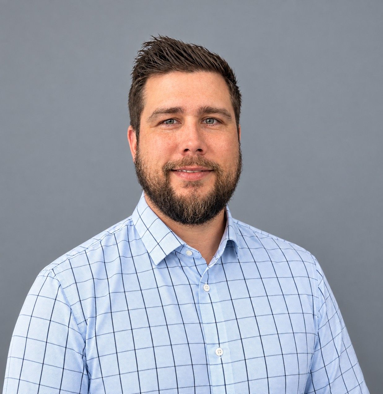 Portrait of a smiling man in a light blue checkered shirt against a gray background