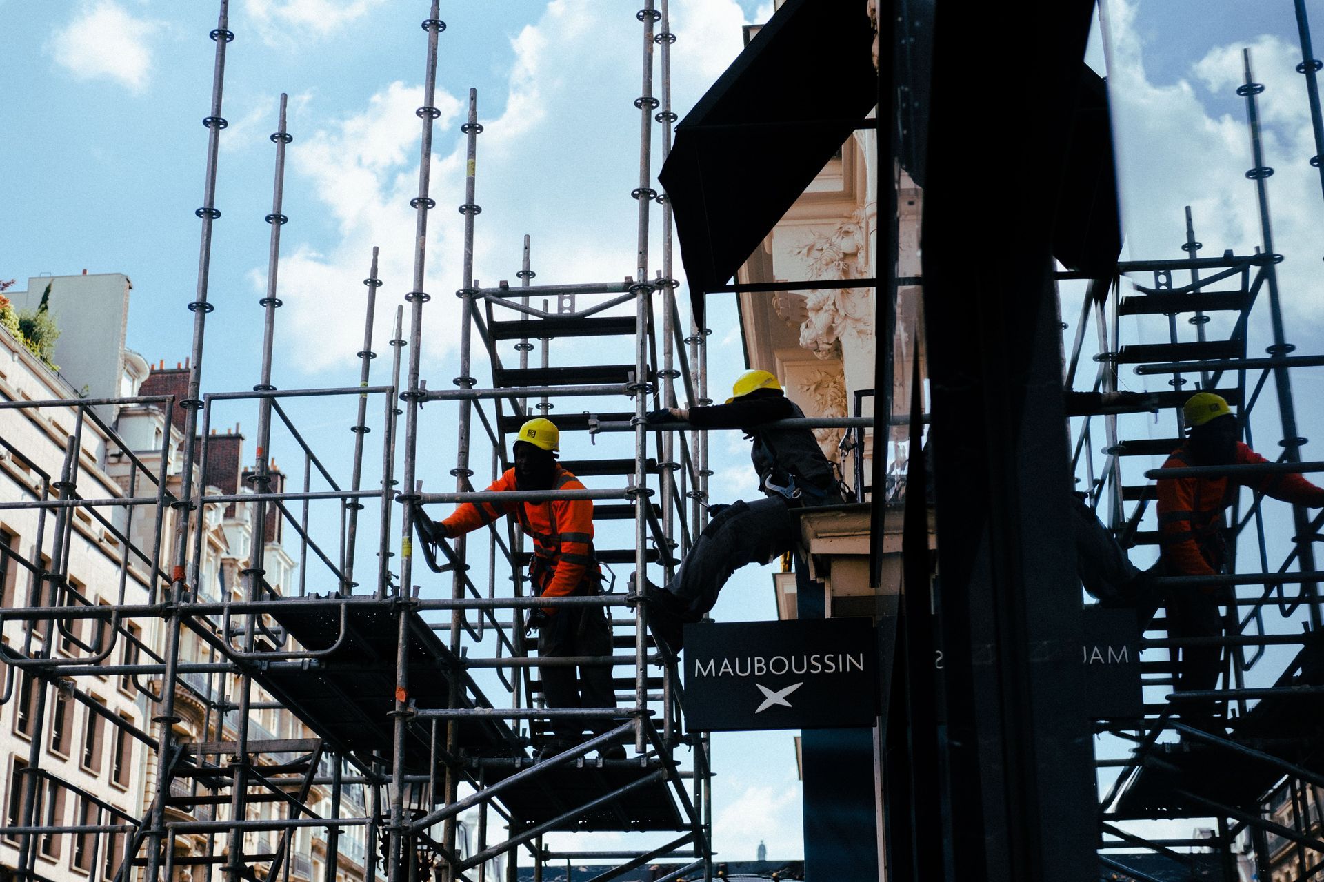 Construction workers on scaffolding around a building under construction, wearing hard hats and safety gear