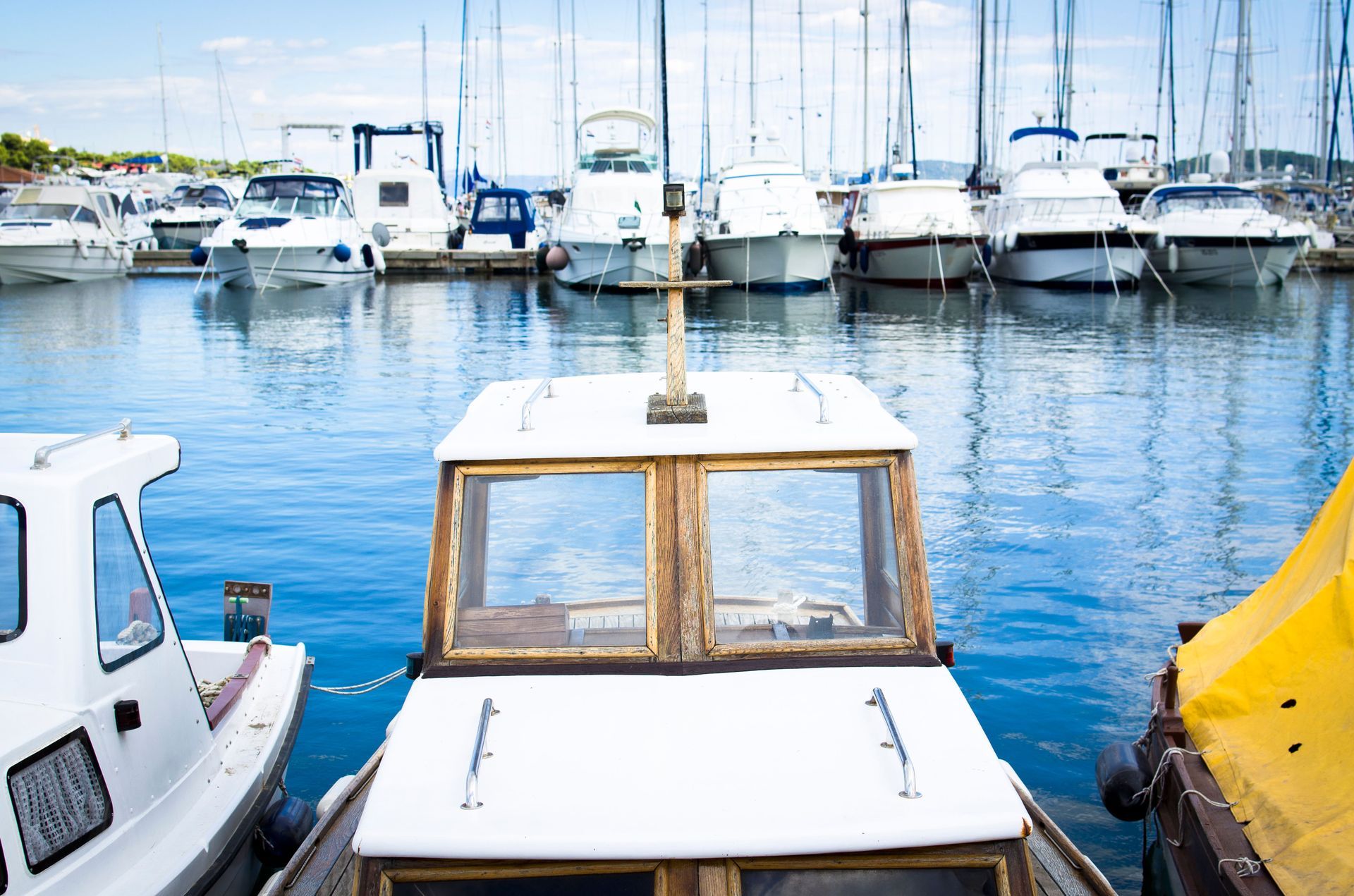 Small boats docked in a marina with sailboats and calm blue water behind them