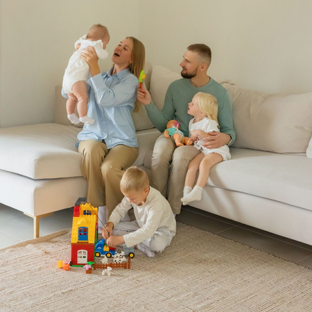 Family playing on a light gray couch and carpet with colorful toys in a bright living room