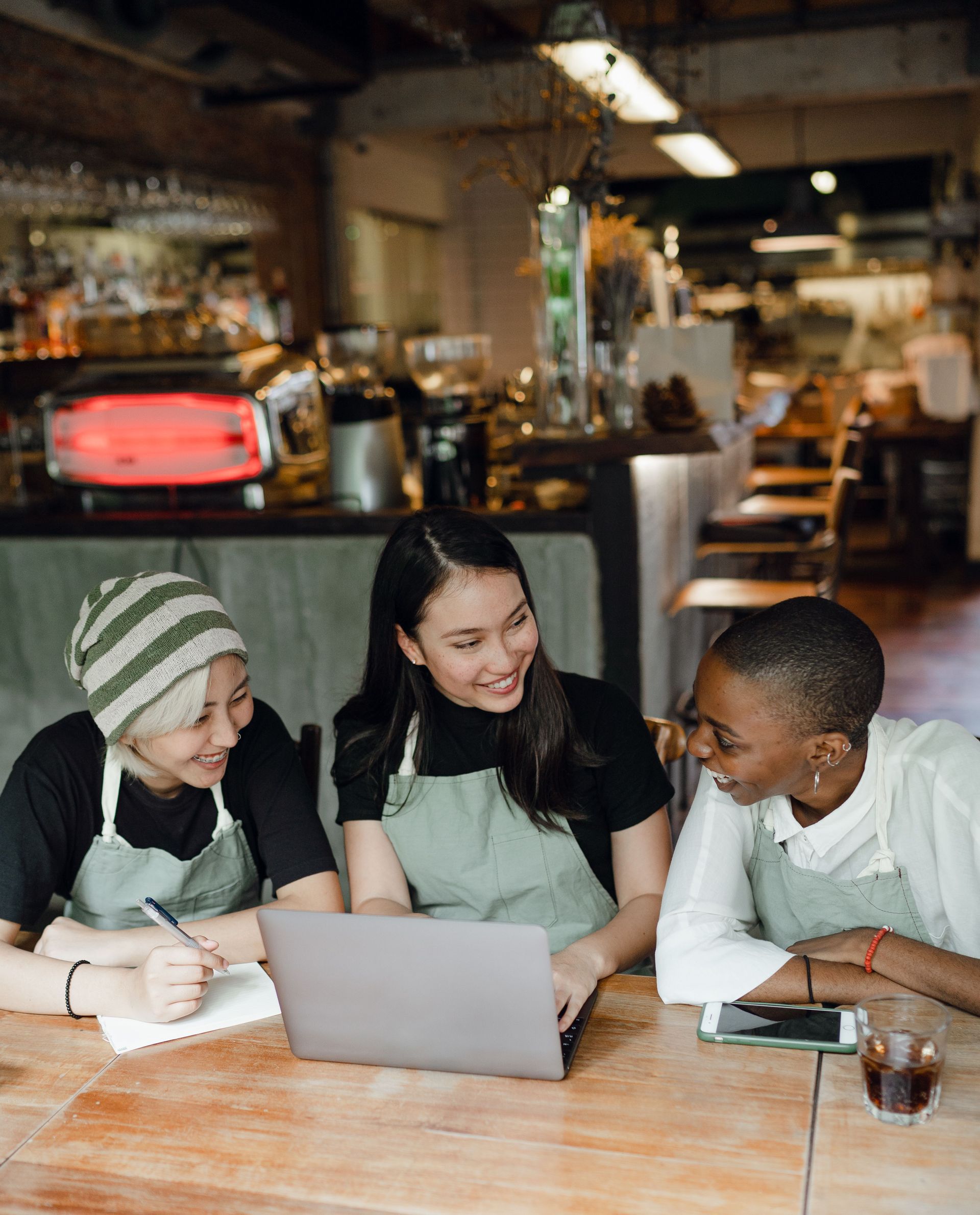 Three coworkers smiling around a laptop in a cozy café workspace